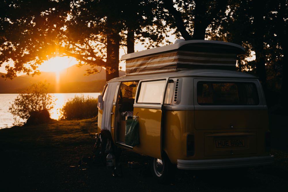 Brown RV under a tree and by a lake at sunset. Photo by Kevin Schmid on Unsplash.